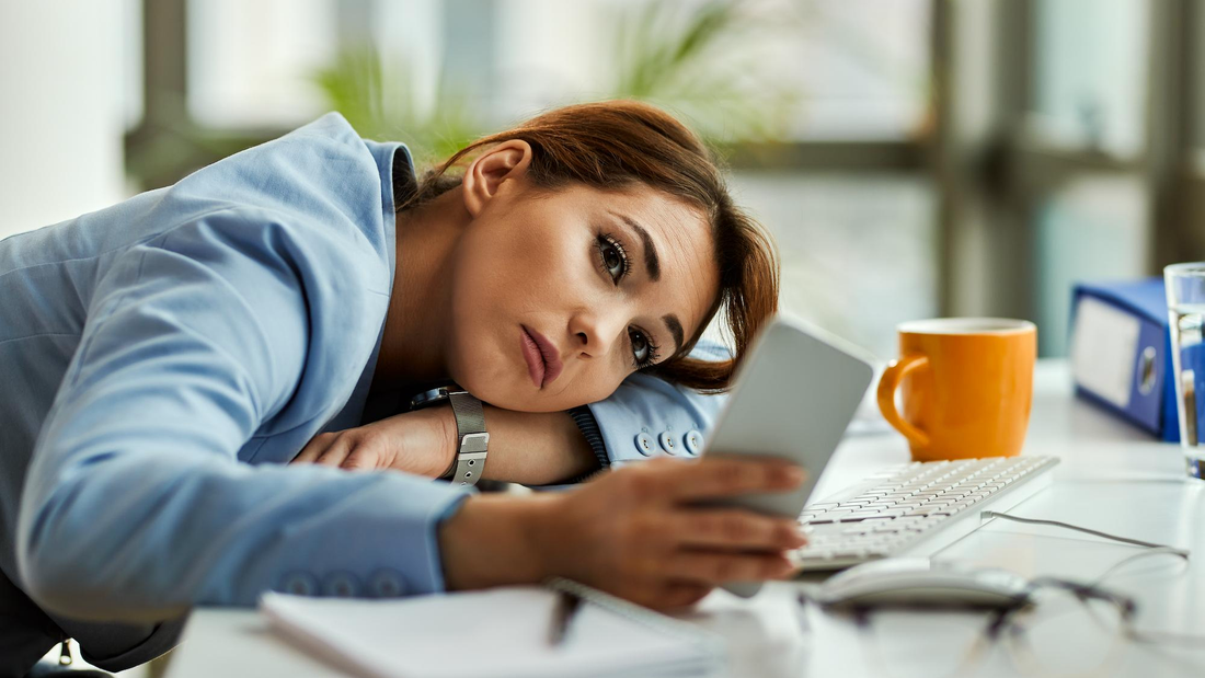 Nachdenkliche Geschäftsfrau, die im Büro entspannt ihr Mobiltelefon benutzt