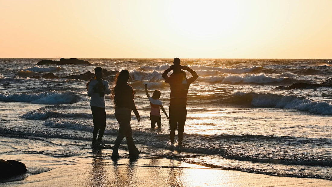 A family of five walking along the shore of a beach.
