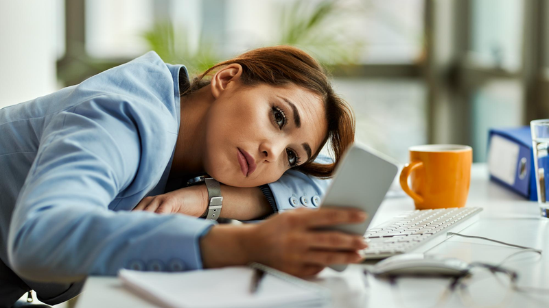 Nachdenkliche Geschäftsfrau, die im Büro entspannt ihr Mobiltelefon benutzt